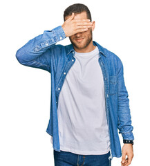 Young caucasian man wearing casual clothes covering eyes with hand, looking serious and sad. sightless, hiding and rejection concept