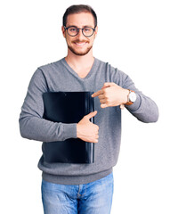 Young handsome caucasian man holding business folder smiling happy pointing with hand and finger