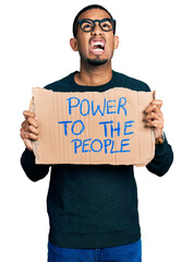 Young african american man holding power to the people banner angry and mad screaming frustrated and furious, shouting with anger looking up.