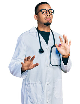 Young african american man wearing doctor uniform and stethoscope afraid and terrified with fear expression stop gesture with hands, shouting in shock. panic concept.