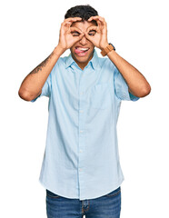 Fototapeta premium Young handsome african american man wearing casual clothes doing ok gesture like binoculars sticking tongue out, eyes looking through fingers. crazy expression.