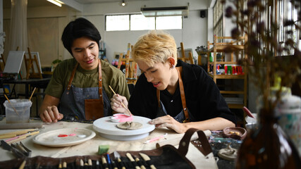 Joyful young asian man are creating handmade ceramics, shaping and decorating pottery in workshop