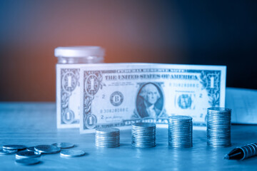 Stack of money coin and dollars banknotes on office desk. Business and financial concept with blue filter