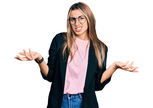 Hispanic young woman wearing business jacket and glasses clueless and confused with open arms, no idea concept.