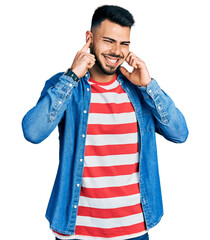 Young hispanic man with beard wearing casual denim jacket covering ears with fingers with annoyed...
