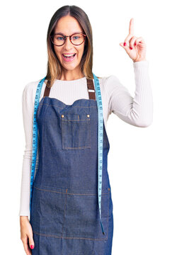 Beautiful brunette young woman dressmaker designer wearing atelier apron pointing finger up with successful idea. exited and happy. number one.