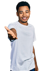 Young african american man wearing casual white t shirt smiling cheerful offering palm hand giving assistance and acceptance.