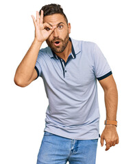 Handsome man with beard wearing casual clothes doing ok gesture shocked with surprised face, eye looking through fingers. unbelieving expression.