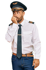 Handsome man with beard wearing airplane pilot uniform looking stressed and nervous with hands on mouth biting nails. anxiety problem.