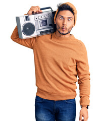 Handsome latin american young man holding boombox, listening to music making fish face with lips, crazy and comical gesture. funny expression.