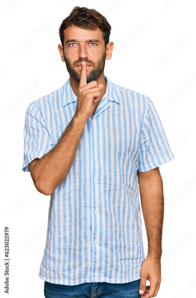 Sticker Handsome young man with beard wearing casual fresh shirt asking to be quiet with finger on lips. silence and secret concept.