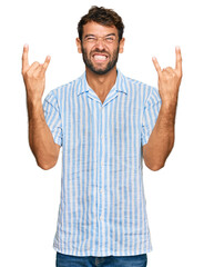 Handsome young man with beard wearing casual fresh shirt shouting with crazy expression doing rock symbol with hands up. music star. heavy concept.