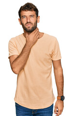 Handsome young man with beard wearing casual tshirt touching painful neck, sore throat for flu, clod and infection