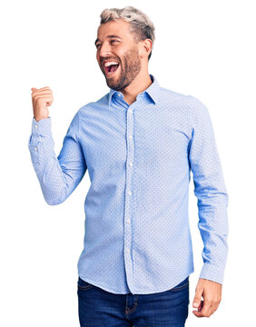 Young handsome blond man wearing elegant shirt smiling with happy face looking and pointing to the side with thumb up.