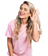 Young blonde woman wearing casual pink t shirt smiling with hand over ear listening and hearing to rumor or gossip. deafness concept.
