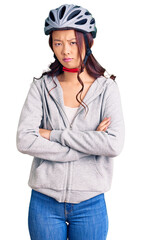 Young beautiful chinese girl wearing bike helmet skeptic and nervous, disapproving expression on face with crossed arms. negative person.