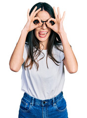 Obraz na płótnie Canvas Young hispanic woman wearing casual clothes and glasses doing ok gesture like binoculars sticking tongue out, eyes looking through fingers. crazy expression.