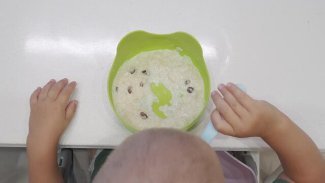 toddler child eats rice milk porridge with fruit pieces at dining table in kitchen
