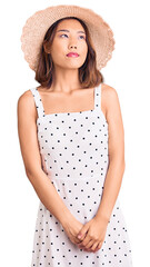 Young beautiful chinese girl wearing summer hat smiling looking to the side and staring away thinking.