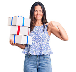 Young beautiful brunette woman holding birthday gift pointing finger to one self smiling happy and proud