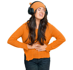 Beautiful brunette young woman listening to music using headphones with hand on stomach because nausea, painful disease feeling unwell. ache concept.