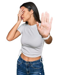 Obraz na płótnie Canvas Young hispanic girl wearing casual white t shirt covering eyes with hands and doing stop gesture with sad and fear expression. embarrassed and negative concept.