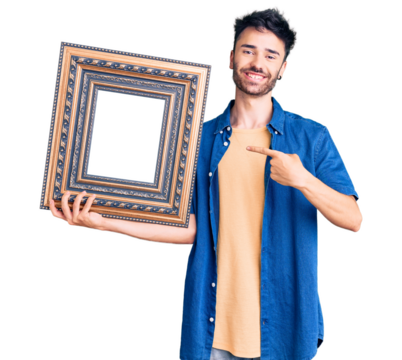 Young hispanic man holding empty frame smiling happy pointing with hand and finger