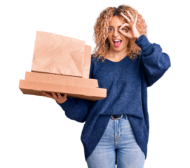 Young blonde woman with curly hair holding delivery food smiling happy doing ok sign with hand on eye looking through fingers