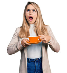 Young blonde woman wearing business style drinking cup of coffee angry and mad screaming frustrated and furious, shouting with anger looking up.
