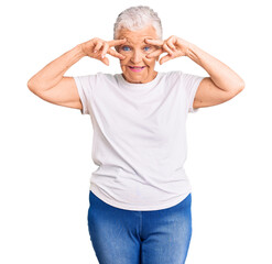 Senior beautiful woman with blue eyes and grey hair wearing casual white tshirt doing peace symbol with fingers over face, smiling cheerful showing victory