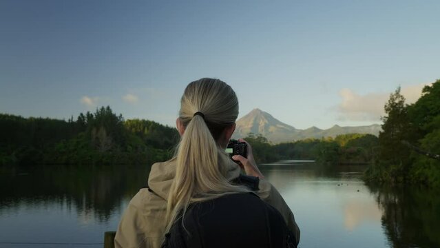 Blond female photographer taking nature landscape picture of lake and distant volcano
