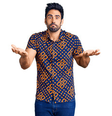 Handsome hispanic man wearing casual clothes clueless and confused expression with arms and hands...