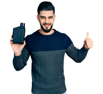 Young arab man with beard holding motor oil bottle smiling happy and positive, thumb up doing excellent and approval sign