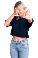 Young beautiful blonde woman wearing casual t-shirt covering eyes with hands and doing stop gesture with sad and fear expression. embarrassed and negative concept.