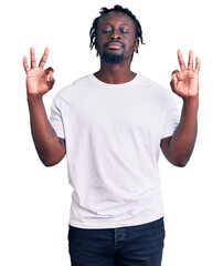 Young african american man with braids wearing casual white tshirt relaxed and smiling with eyes closed doing meditation gesture with fingers. yoga concept.