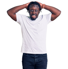 Young african american man with braids wearing casual white tshirt crazy and scared with hands on head, afraid and surprised of shock with open mouth