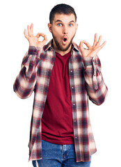 Naklejka premium Young handsome man wearing casual shirt looking surprised and shocked doing ok approval symbol with fingers. crazy expression