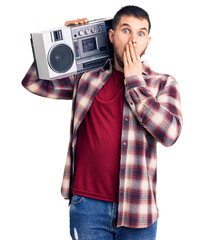 Young handsome man listening to music holding boombox covering mouth with hand, shocked and afraid...