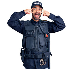 Young hispanic man wearing police uniform doing peace symbol with fingers over face, smiling cheerful showing victory