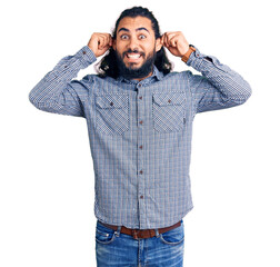 Young arab man wearing casual clothes smiling pulling ears with fingers, funny gesture. audition...