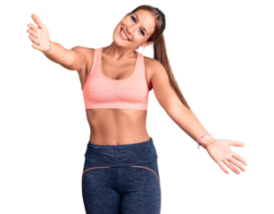 Young beautiful hispanic woman wearing sportswear looking at the camera smiling with open arms for hug. cheerful expression embracing happiness.