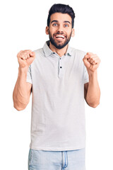 Young handsome man with beard wearing casual polo celebrating surprised and amazed for success with arms raised and open eyes. winner concept.