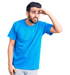 Fototapeta premium Young handsome man with beard wearing casual t-shirt very happy and smiling looking far away with hand over head. searching concept.