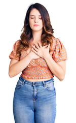 Beautiful young brunette woman wearing casual clothes smiling with hands on chest with closed eyes and grateful gesture on face. health concept.