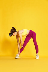 Fototapeta na wymiar Full-length image of young slim woman wearing vr glases and training against yellow studio background. Warming-up, stretching. Concept of sport, fitness, body care, fashion, youth, lifestyle, ad