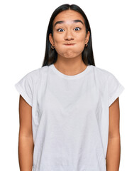 Young asian woman wearing casual white t shirt puffing cheeks with funny face. mouth inflated with air, crazy expression. - obrazy, fototapety, plakaty