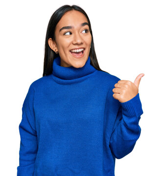 Young asian woman wearing casual winter sweater smiling with happy face looking and pointing to the side with thumb up.
