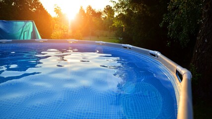 Swimming pool with metal frame for home and garden. Frame swimming pool in the yard. Garden in the background. Summer holiday fun and recreation.