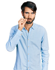 Hispanic man with blue eyes wearing business shirt mouth and lips shut as zip with fingers. secret and silent, taboo talking