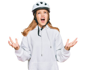 Beautiful young caucasian girl wearing bike helmet crazy and mad shouting and yelling with aggressive expression and arms raised. frustration concept.